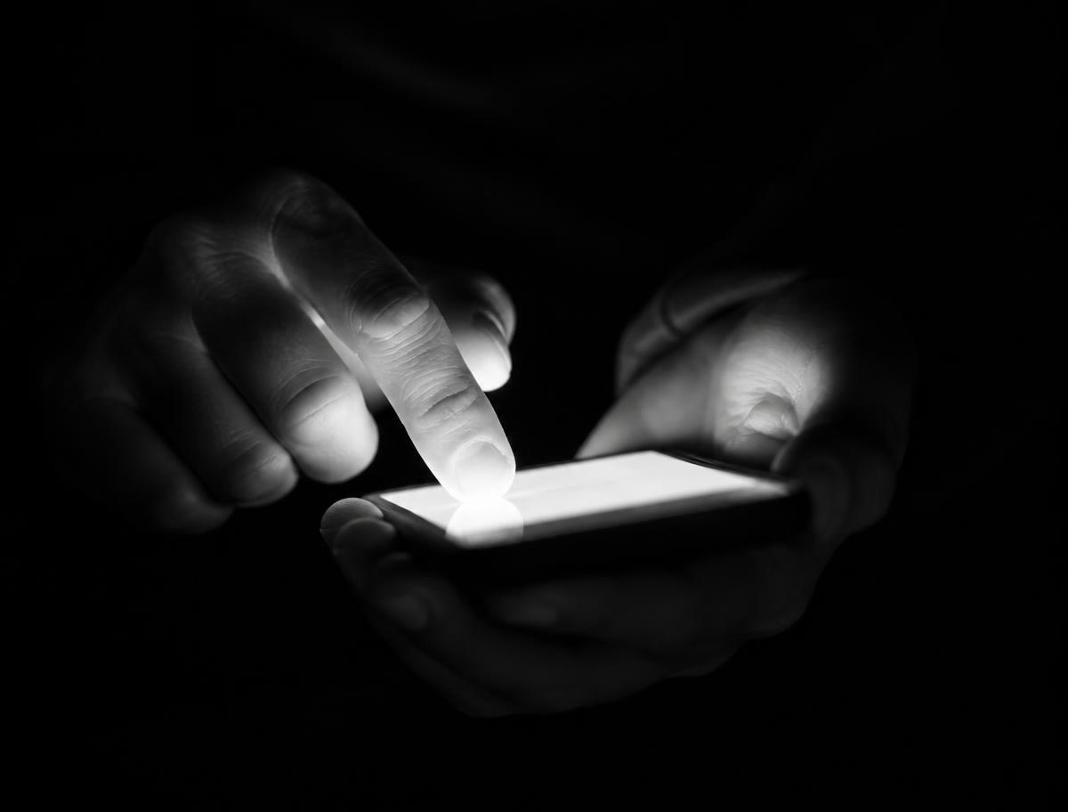 Hands holding a phone in low light, no face shown, representing starting a digital operation from a phone.